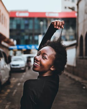 Black woman with curly hair smiling on a city street with a playful pose.