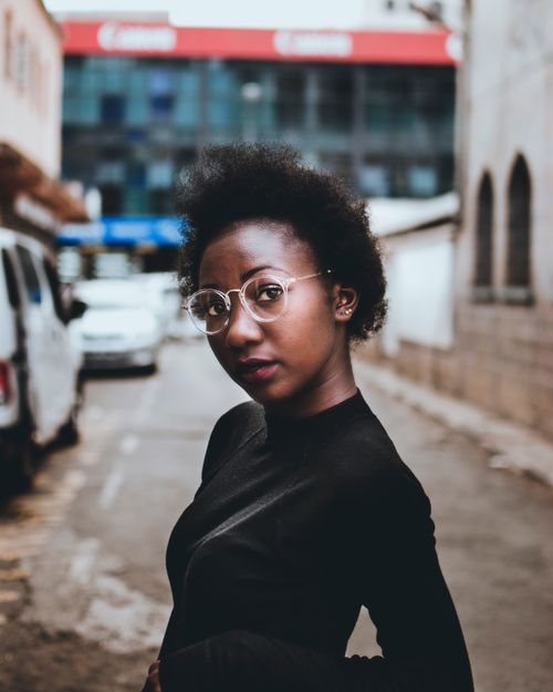 Free Portrait of a fashionable woman with eyeglasses posing confidently in an urban street scene. Stock Photo