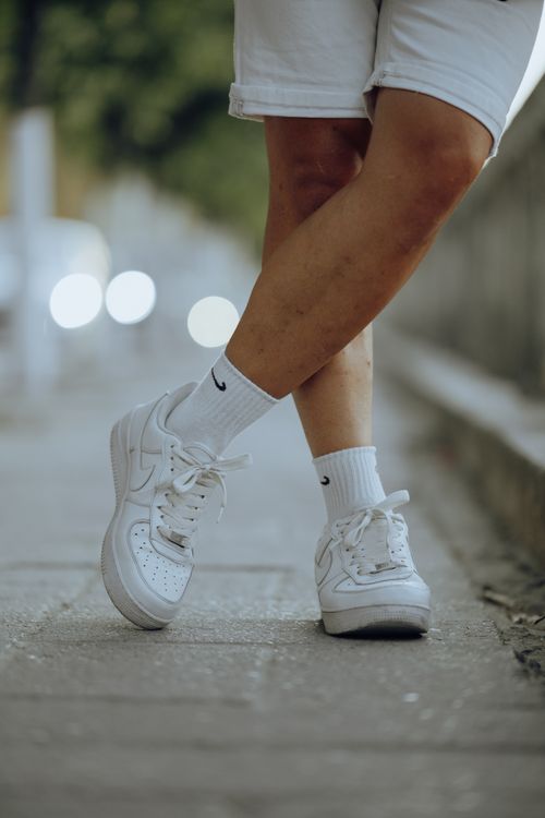 Free Close-up of legs wearing white sneakers and shorts on an urban pavement. Stock Photo