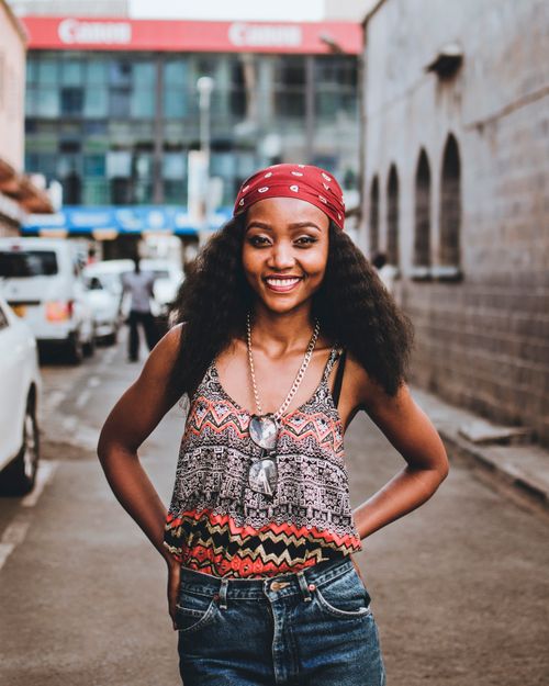 Free A trendy woman smiling confidently on a street with a fashion-forward style and colorful attire. Stock Photo
