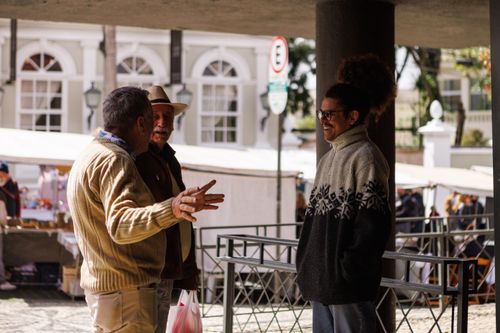 Free Three men casually chatting in an outdoor market in Curitiba, Brazil, captured during a sunny day. Stock Photo