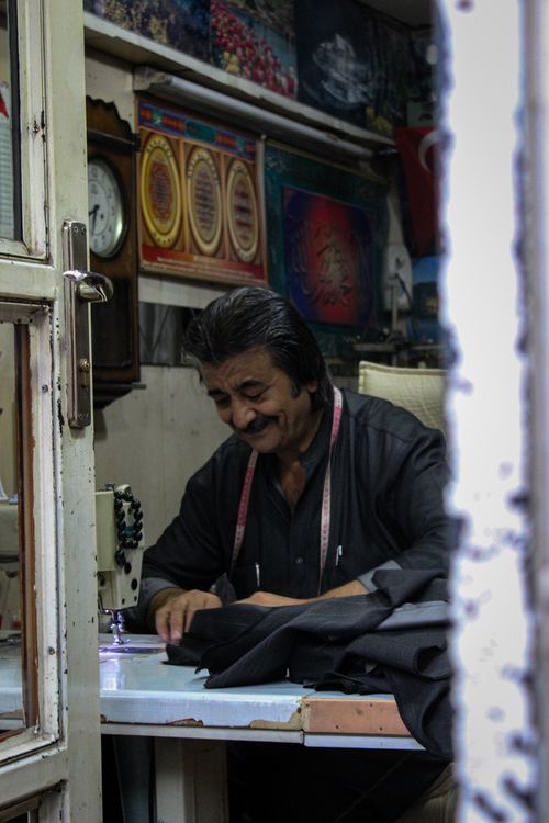 Free A tailor smiles while sewing garments in his workshop, creating a warm and inviting atmosphere. Stock Photo