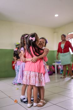 Joyful moment of young schoolgirls embracing in a colorful indoor classroom setting.