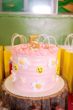 Pink cake for a 5th birthday party with floral and smiley face decorations.