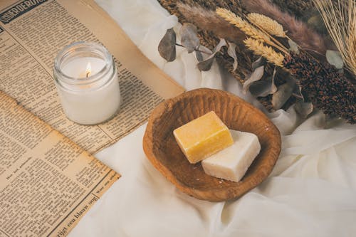 Soap Bars in a Bowl Standing next to Dried Flowers, a Candle and Old Newspapers 