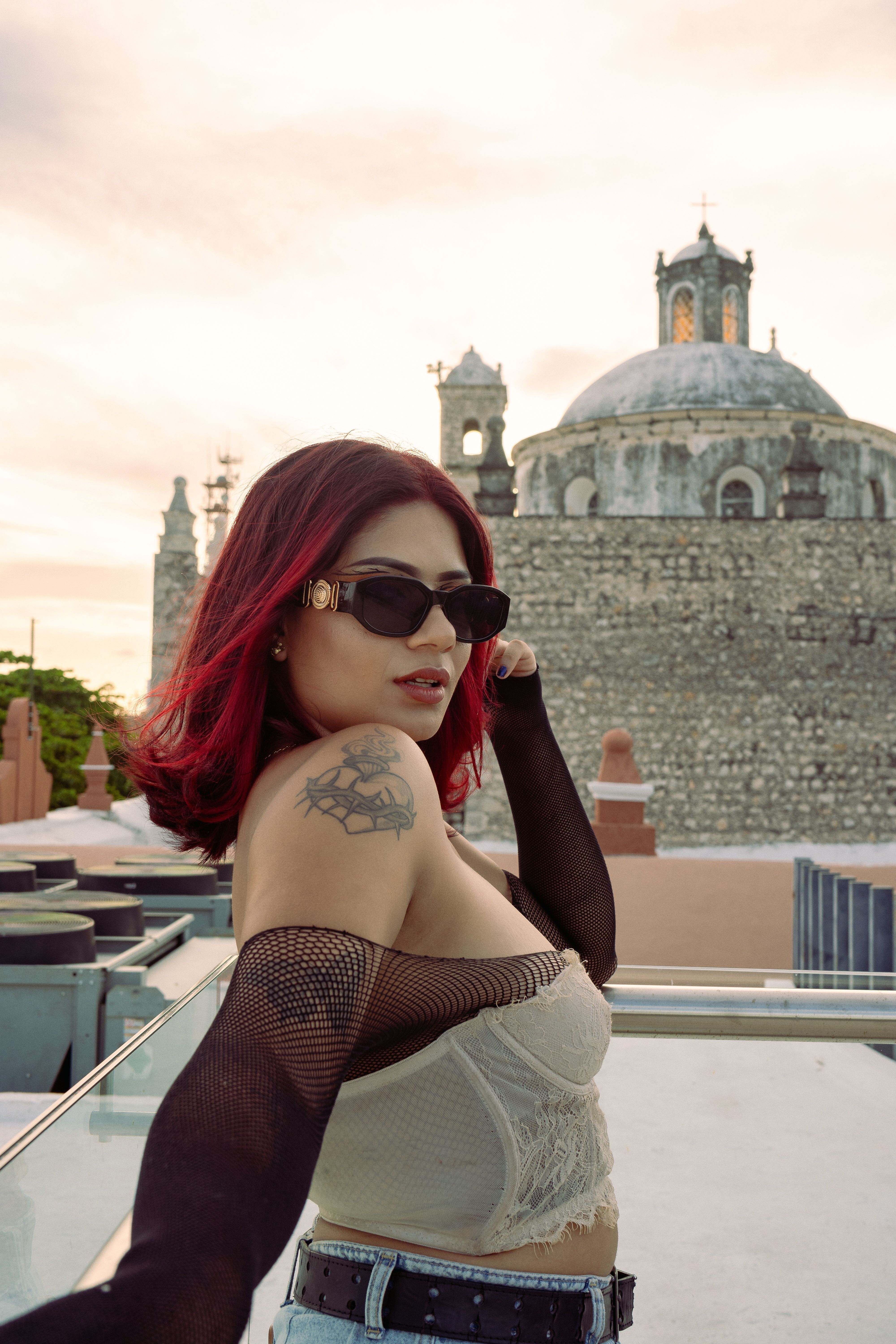 Trendy woman with red hair and tattoos poses in Mérida, Mexico, with historical architecture in the backdrop.