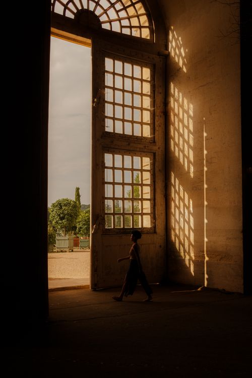 Free A child walks through a large arched doorway with soft golden lighting casting intricate shadows. Stock Photo