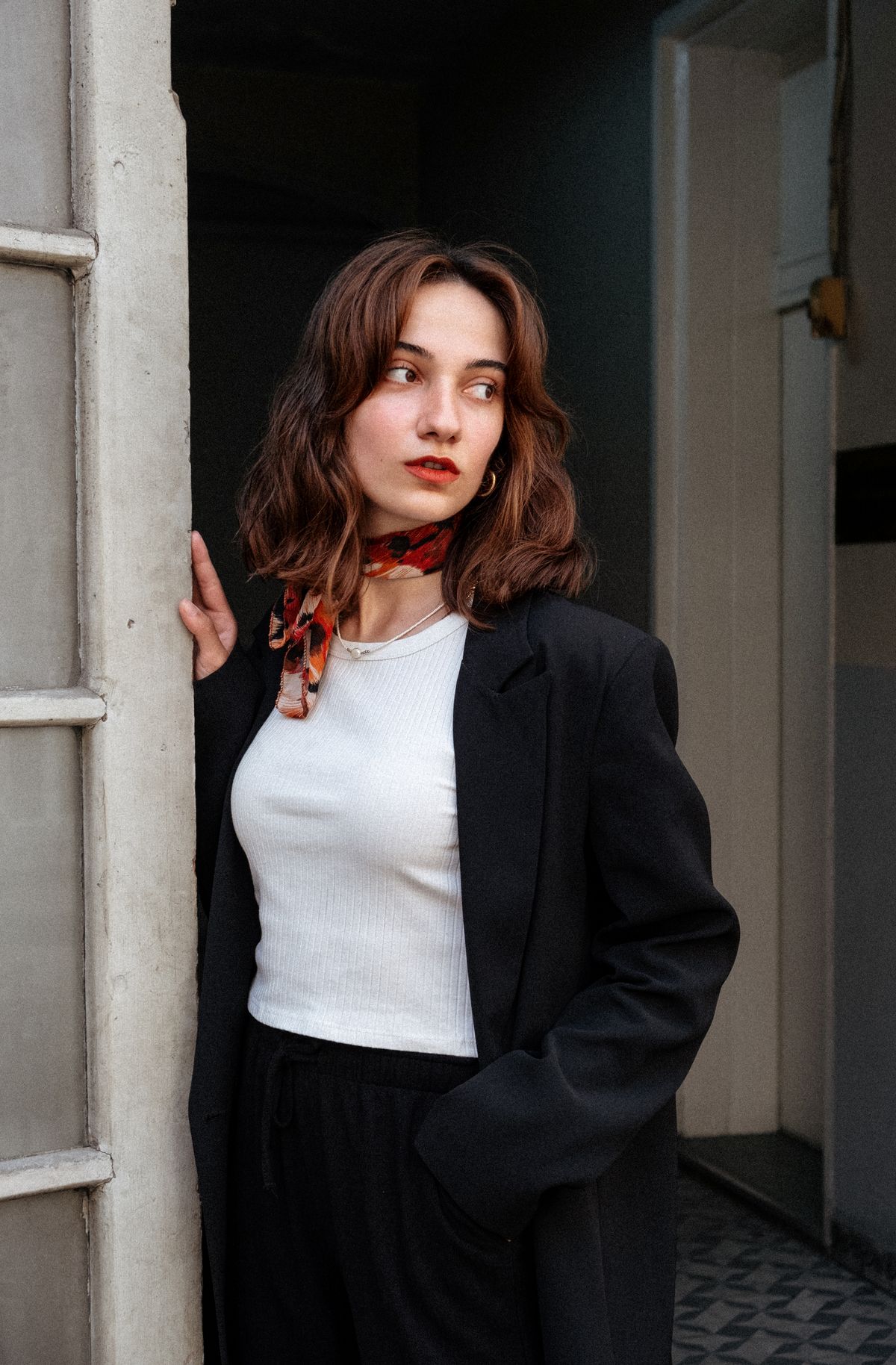 Statement Scarf Outfits for Women — 7 Ways to Style a Scarf as the Star Woman in a black blazer and scarf leaning against a doorframe