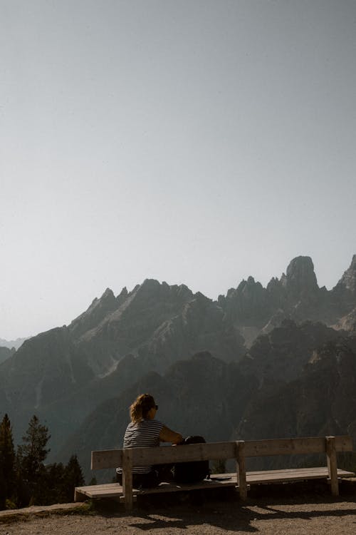 Woman Sitting on Bench with Rocky Mountains behind