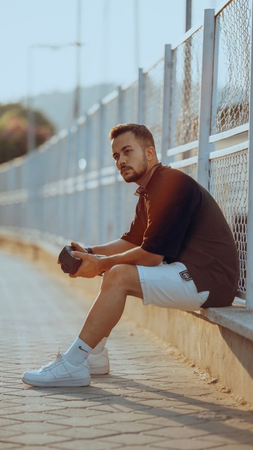 Free A young man wearing casual black and white attire sits pensively on a sidewalk. Stock Photo