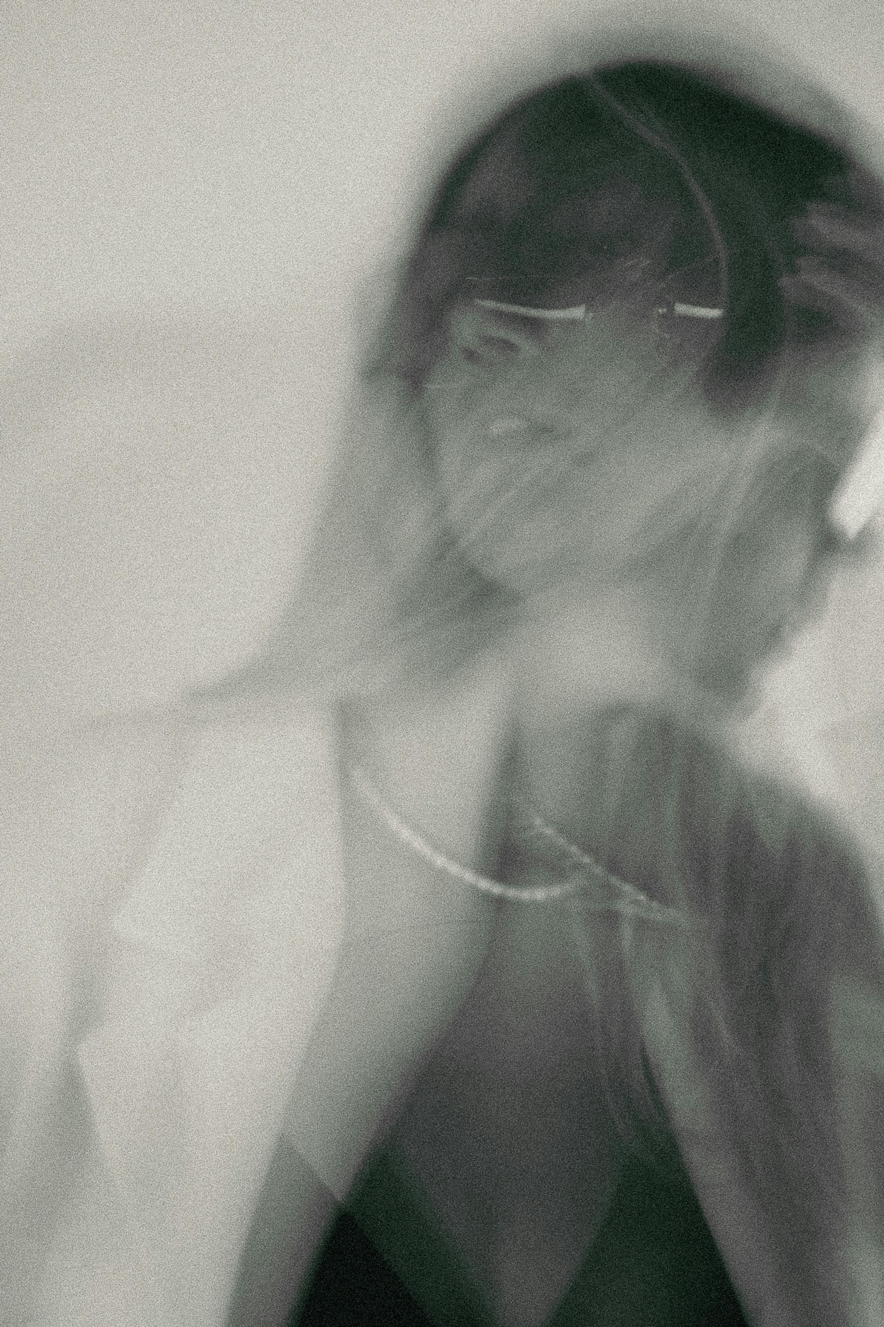 Artistic blurred portrait of a woman with eyeglasses and necklace, using double exposure technique.