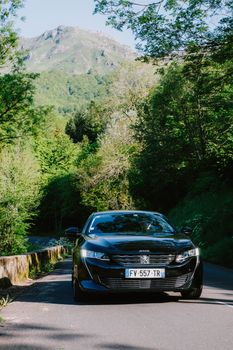 Modern car driving along a lush mountain road with summer greenery.