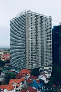 A tall skyscraper stands above a bustling urban area with residential buildings.