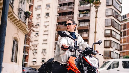 Free Confident woman in sunglasses riding motorcycle in vibrant city setting. Stock Photo