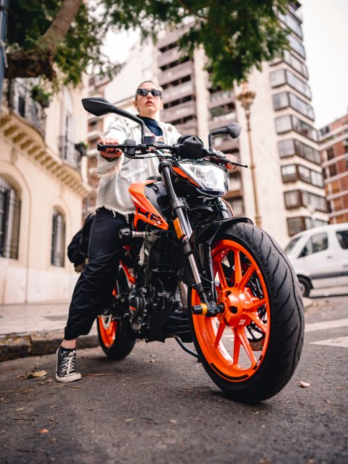 Free Stylish urban biker wearing sunglasses poses with a black and orange motorcycle on a city street. Stock Photo