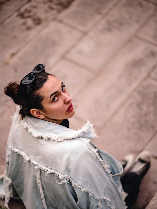 Free Fashionable woman wearing a jean jacket and sunglasses, seated outdoors. Stock Photo