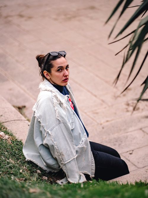 Free Young woman in a jean jacket sitting outdoors, exhibiting urban fashion style. Stock Photo