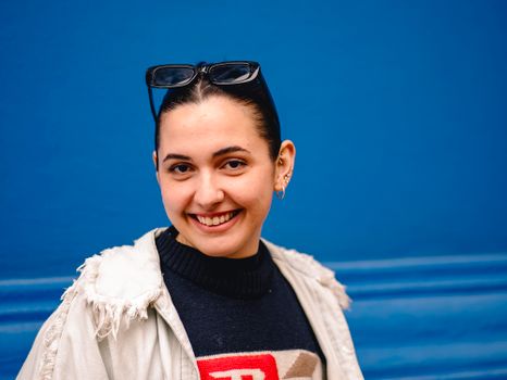 Portrait of smiling woman wearing sunglasses on head against a vibrant blue wall.