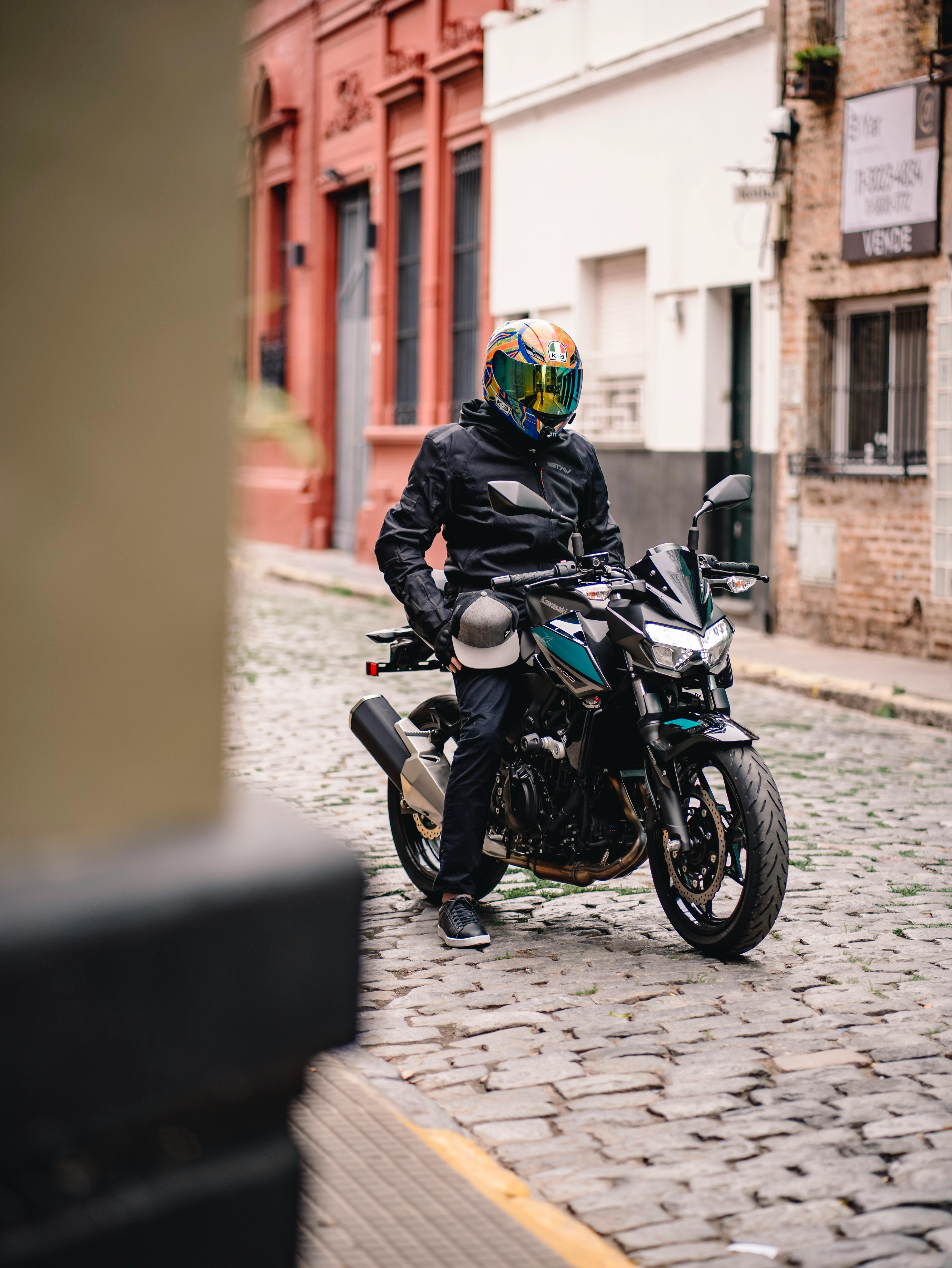 Free A motorcyclist wearing a helmet and jacket on a cobblestone street in an urban setting. Stock Photo