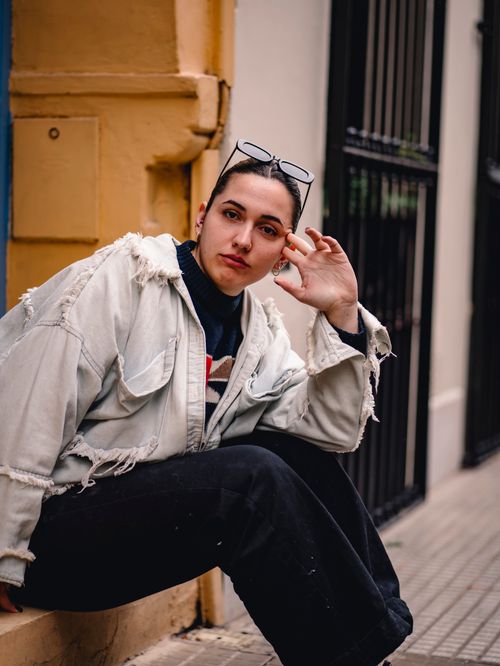 Free A stylish woman in a ripped denim jacket sitting outdoors in an urban environment. Stock Photo