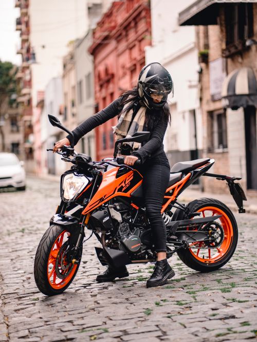 Free Woman wearing helmet and riding a motorcycle on a cobblestone street in the city. Stock Photo
