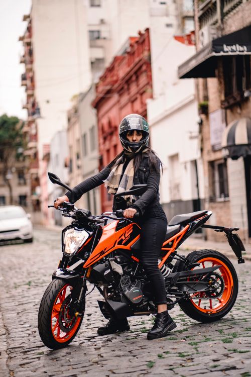 Free A woman stands confidently on a motorcycle in a vibrant urban street. Stock Photo