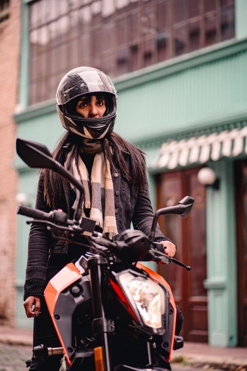 Free Stylish woman wearing a helmet and scarf on a motorcycle in an urban setting. Stock Photo