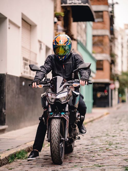 Free A motorcyclist in a helmet and jacket on a cobblestone city street. Stock Photo