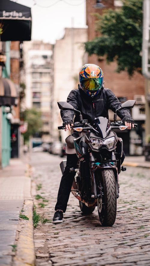 Free A motorcyclist with a colorful helmet rides on a cobblestone street in an urban setting. Stock Photo