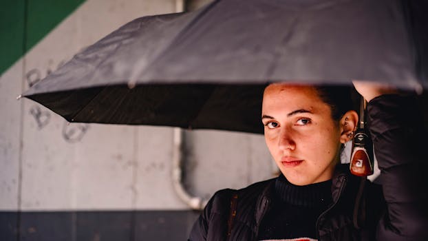 Portrait of a woman holding a black umbrella, captured in an urban environment.