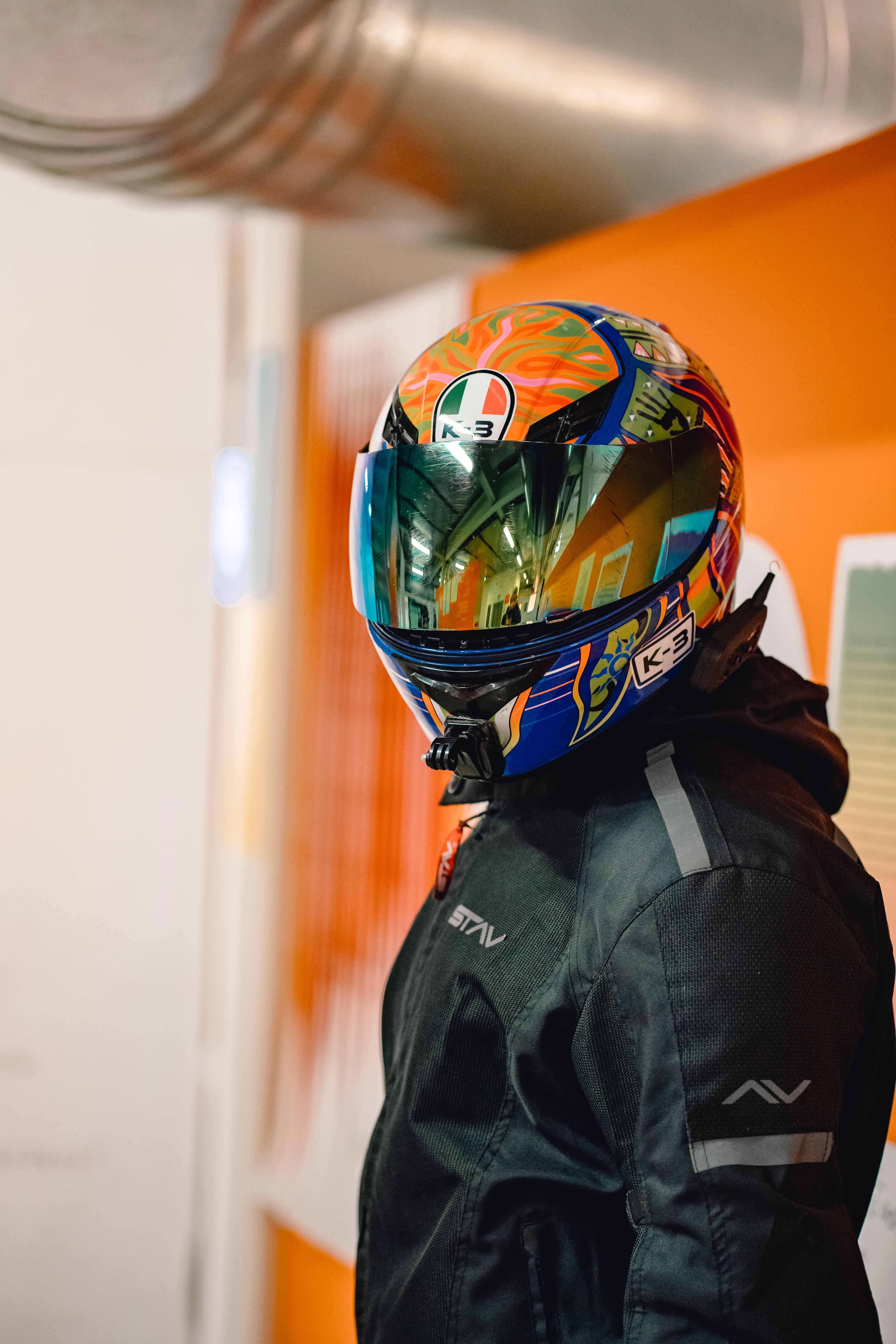 A motorcyclist wearing a vibrant helmet and black jacket indoors.