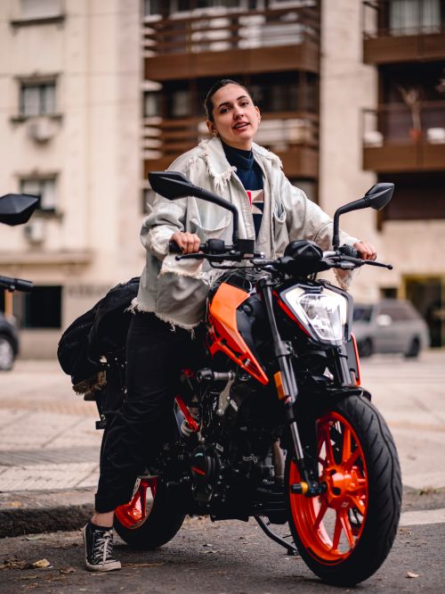 Free Stylish young woman posing on an orange and black motorcycle in an urban setting. Stock Photo