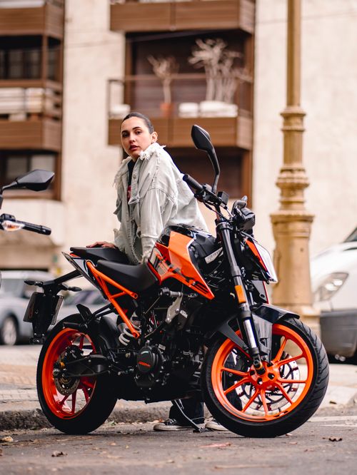 Free Woman in a jean jacket standing next to an orange motorcycle on an urban city street. Stock Photo