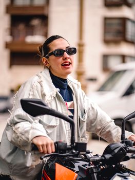 Fashionable young woman in sunglasses posing with a motorcycle on a city street.