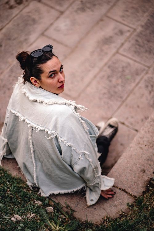 Free Young woman sitting on steps wearing sunglasses and a frayed denim jacket. Stock Photo