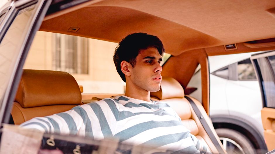 A young man in a striped shirt enjoys comfort in a luxury car, traveling through the city.