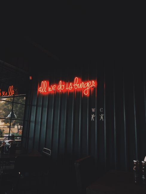 Neon sign in a dimly lit cafe corner reading 'all we do is burger'.