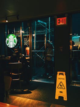 Interior view of a Starbucks with people inside, featuring signage and warm lighting, captured at night.