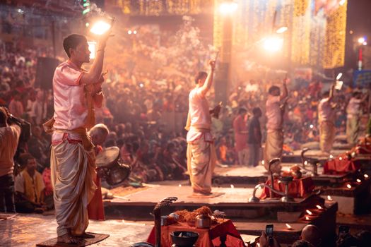 A colorful Hindu ceremony with priests performing rituals amidst a large crowd during a vibrant evening festival.
