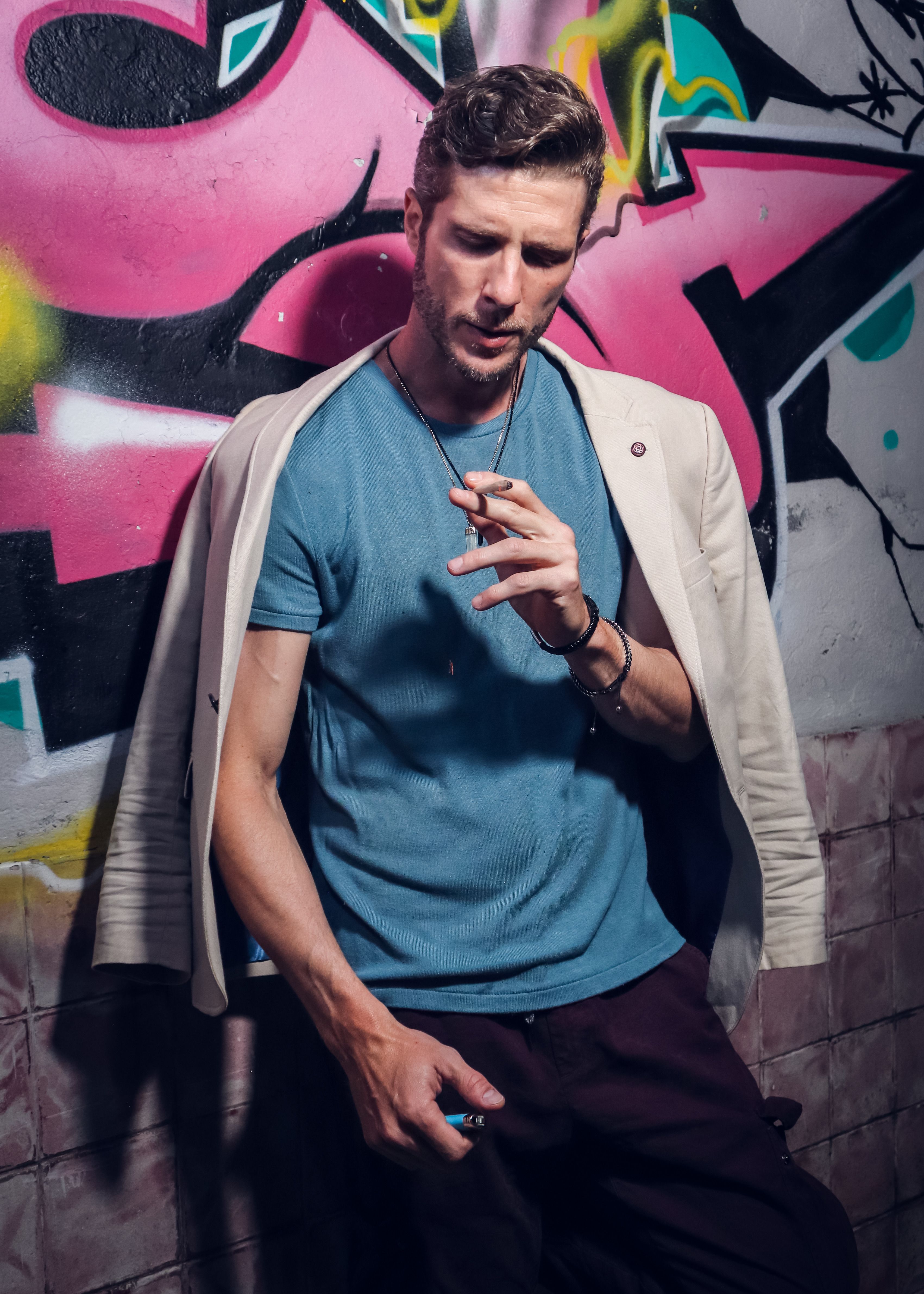 Young man in casual attire posing against colorful graffiti wall in urban area.