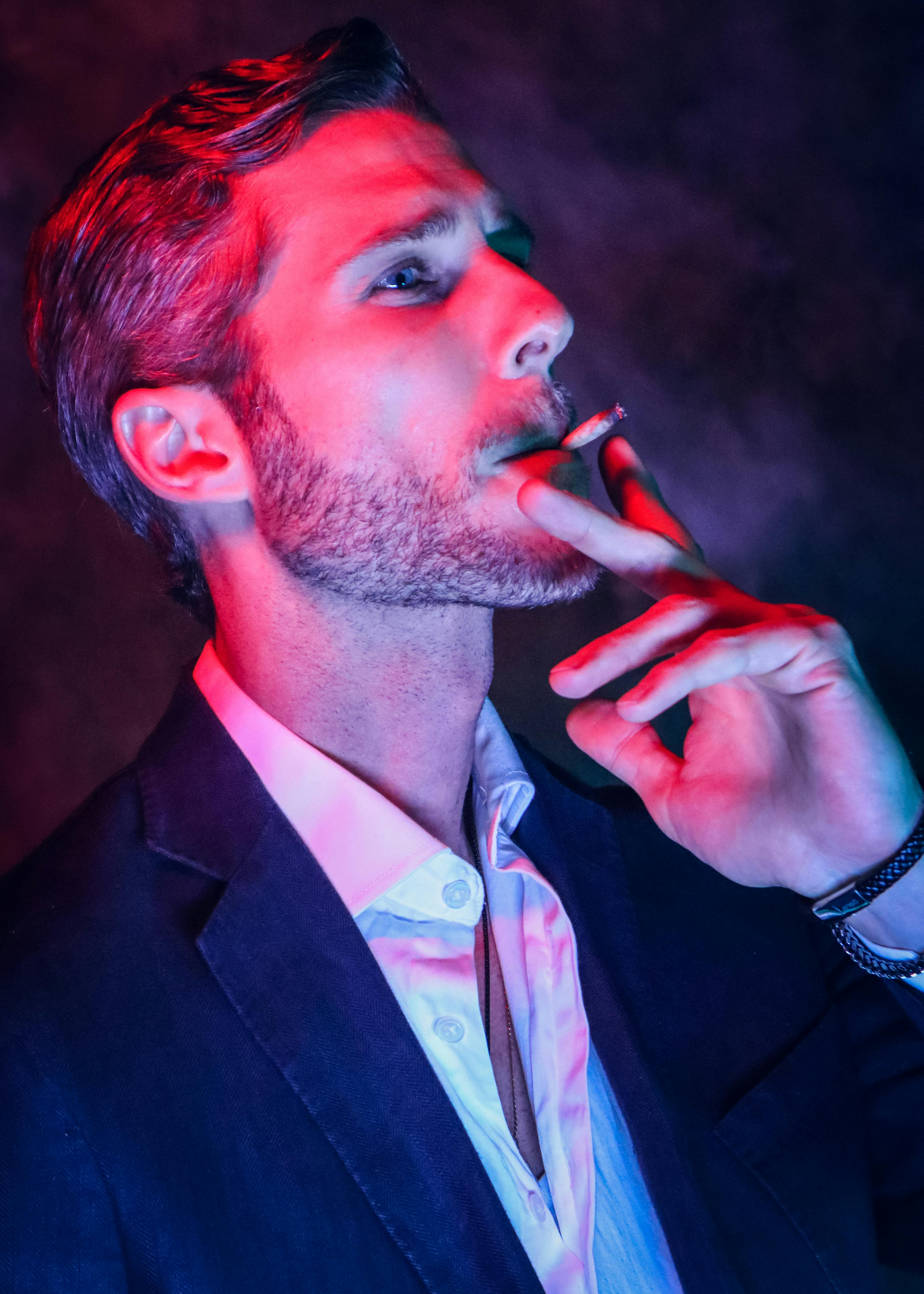 Elegant man in a suit smoking a cigarette, illuminated by vibrant neon lights, exuding a mysterious nightlife vibe.