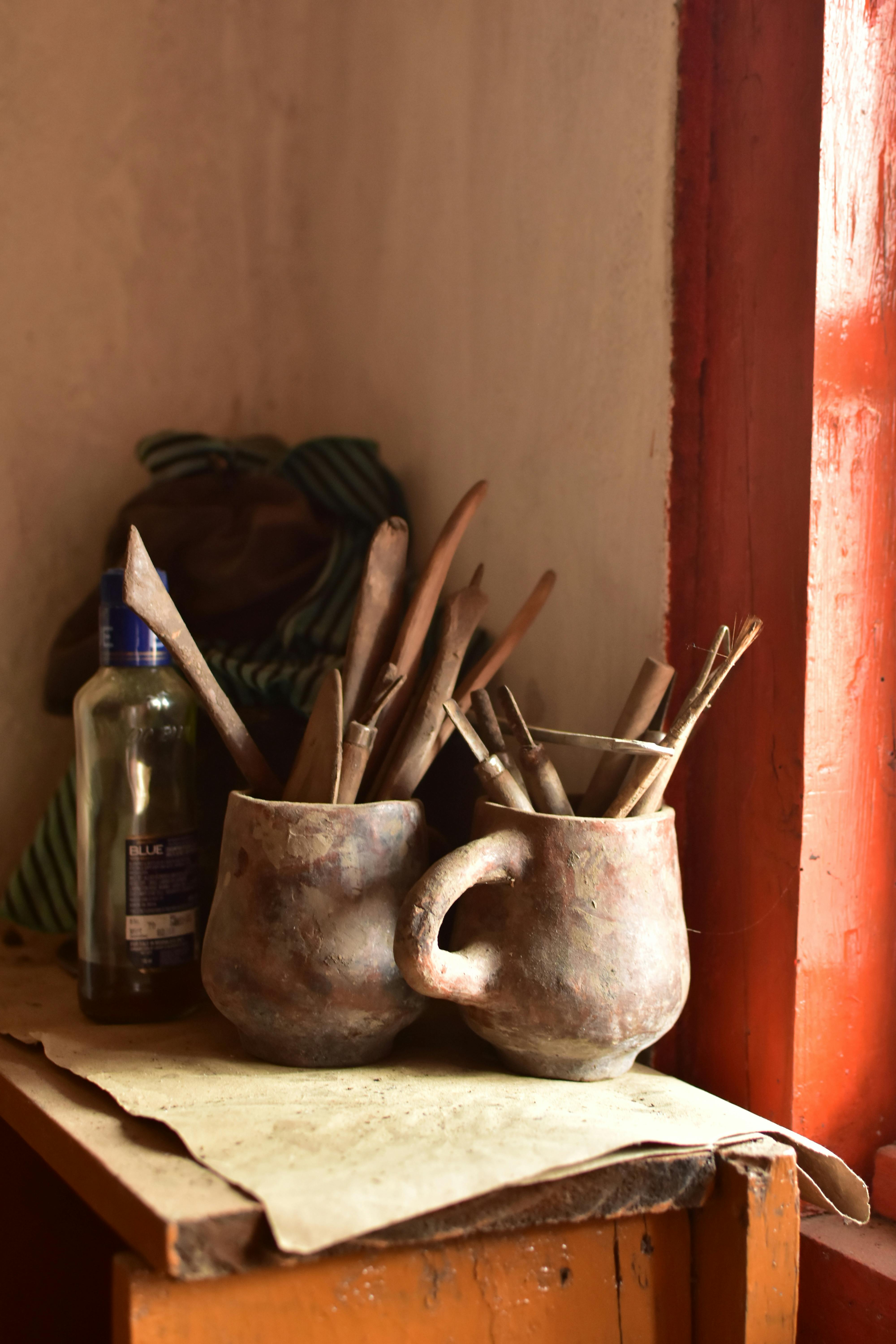 Free Clay mugs filled with tools in a cozy sunlit corner, perfect for art inspiration. Stock Photo