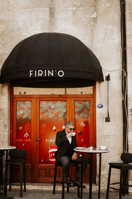 A man in a suit enjoys coffee at an outdoor café with elegant doorway and patio seating.
