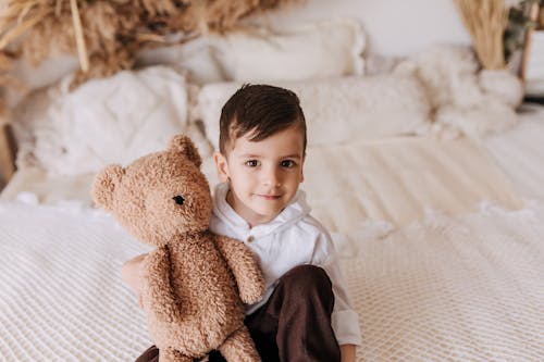 A Little Boy Sitting on the Bed with a Teddy Bear 
