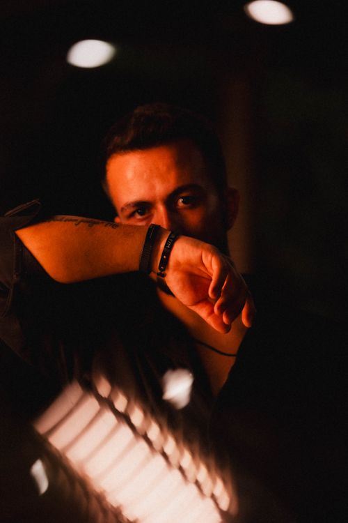 Free Dramatic portrait of an adult man with an arm covering his face, illuminated by red light on a dark background. Stock Photo