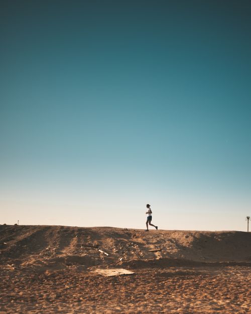 Free A person jogs on a sandy path with a vast blue sky above, capturing movement and freedom. Stock Photo