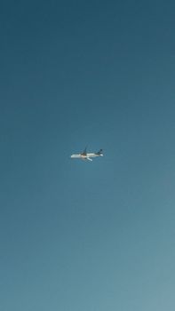 A plane flies through a clear blue sky, captured with aerial perspective.