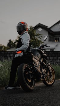 A biker poses with a motorcycle at sunset near a suburban house.