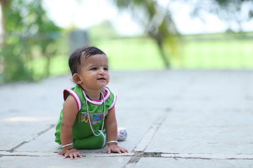 Free Adorable baby in green outfit crawling on outdoor pavement, full of curiosity and charm. Stock Photo
