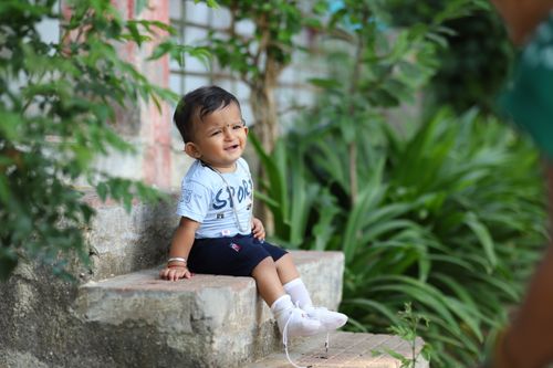 Free Adorable toddler sitting on outdoor concrete steps, smiling cheerfully. Stock Photo